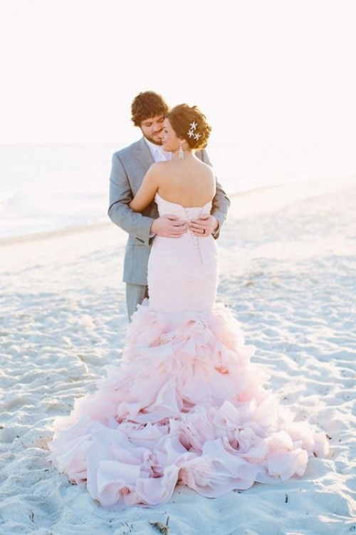 a blush strapless wedding dress with a draped bodice and a pretty ruffle tail for a sweet beach bride