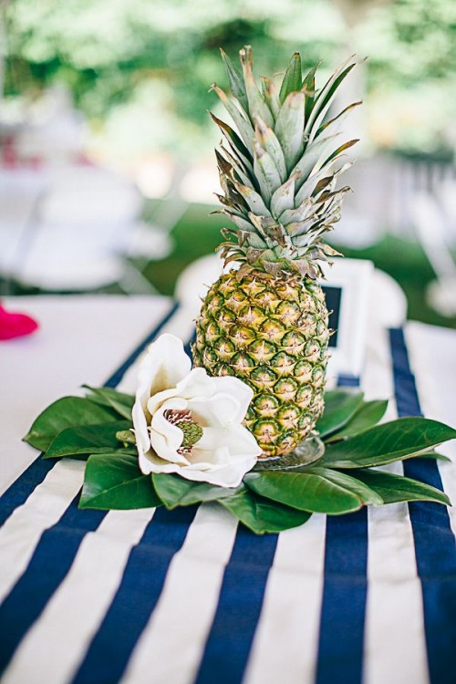a pineapple with leaves and neutral blooms form a great and simple wedding centerpiece for a tropical wedding