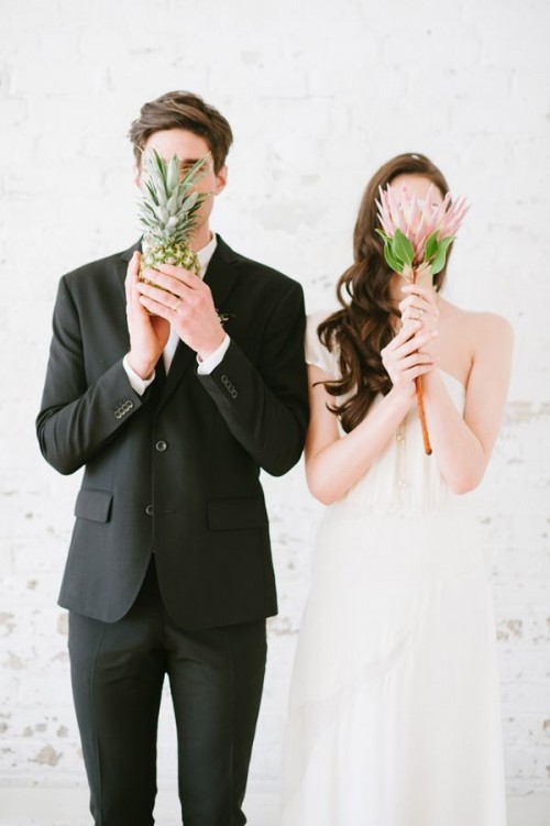 a bride holding a large bloom and a groom holding a pineapple remind that their wedding is a tropical one