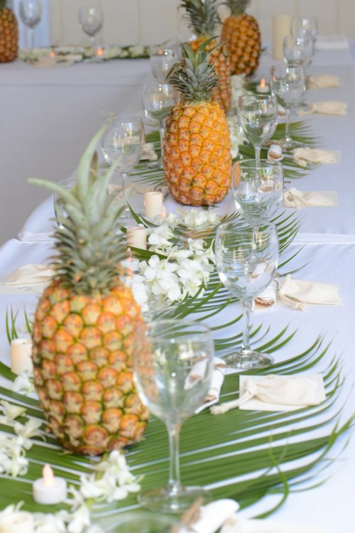 a tropical wedding tablescape with leaves, white tropical blooms and pineapples plus candles is lovely and chic