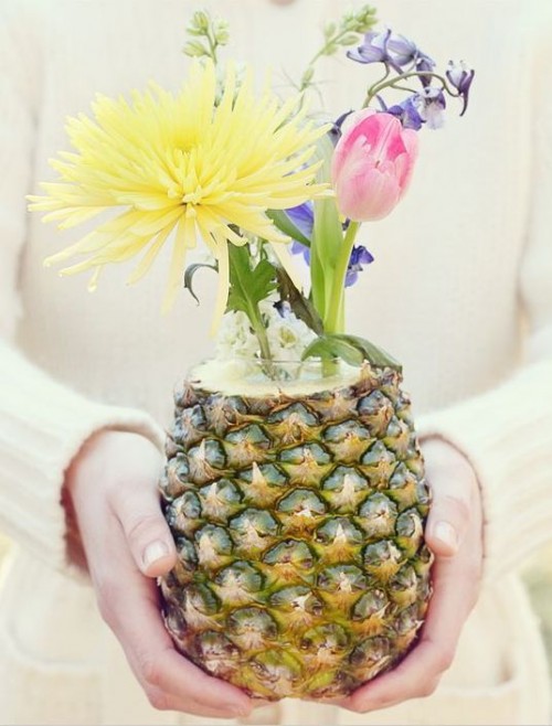 a pineapple as a vase, with bright blooms is a very cool idea for a wedding centerpiece