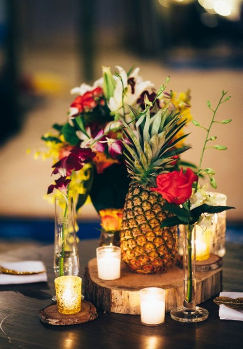 a bright wedding centerpiece of candles, bold blooms and greenery and a pineapple is ideal for a modern and refined tropical wedding