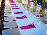 a bold wedding tablescape with fuchsia napkins, pineapples lining up the table and neutral linens