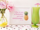 a bright and glam tropical wedding sign with pink printing and a pineapple, pink blooms and a green glass with a pink umbrella for tropical decor