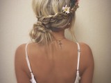 a boho low up with a side braided halo and a low bun plus a bit of fresh blooms tucked into the hair