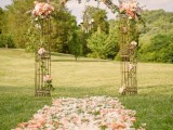 a romantic metal wedding arch decorated with pastel blooms and greenery and with pastel petals covering the aisle