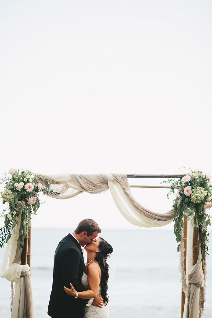 a coastal spring wedding arch decorated with neutral fabric, pink and white blooms and greenery