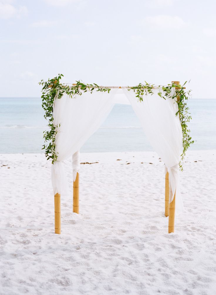 a fresh coastal spring wedding arch decorated with white fabric and greenery on top is classics