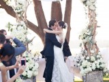 a spring wedding arch made of driftwood and decorated with greenery and lush white blooms for spring