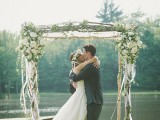 a spring wedding arch composed of branches and decorated with greenery, white blooms and white ribbons all over