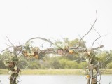 a driftwood spring wedding arch decorated with twigs and greenery and some pastel blooms