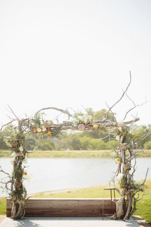 a driftwood spring wedding arch decorated with twigs and greenery and some pastel blooms