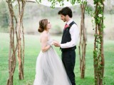 a cool and fresh spring wedding arch made of branches, fresh greenery and some sheer fabric on top looks very spring-like