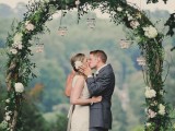 a vine spring wedding arch covered with greenery and white blooms and some candles hanging down is amazing