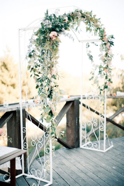 a delicate white metal arch decorated with greenery and peachy blooms feels and looks very spring-like