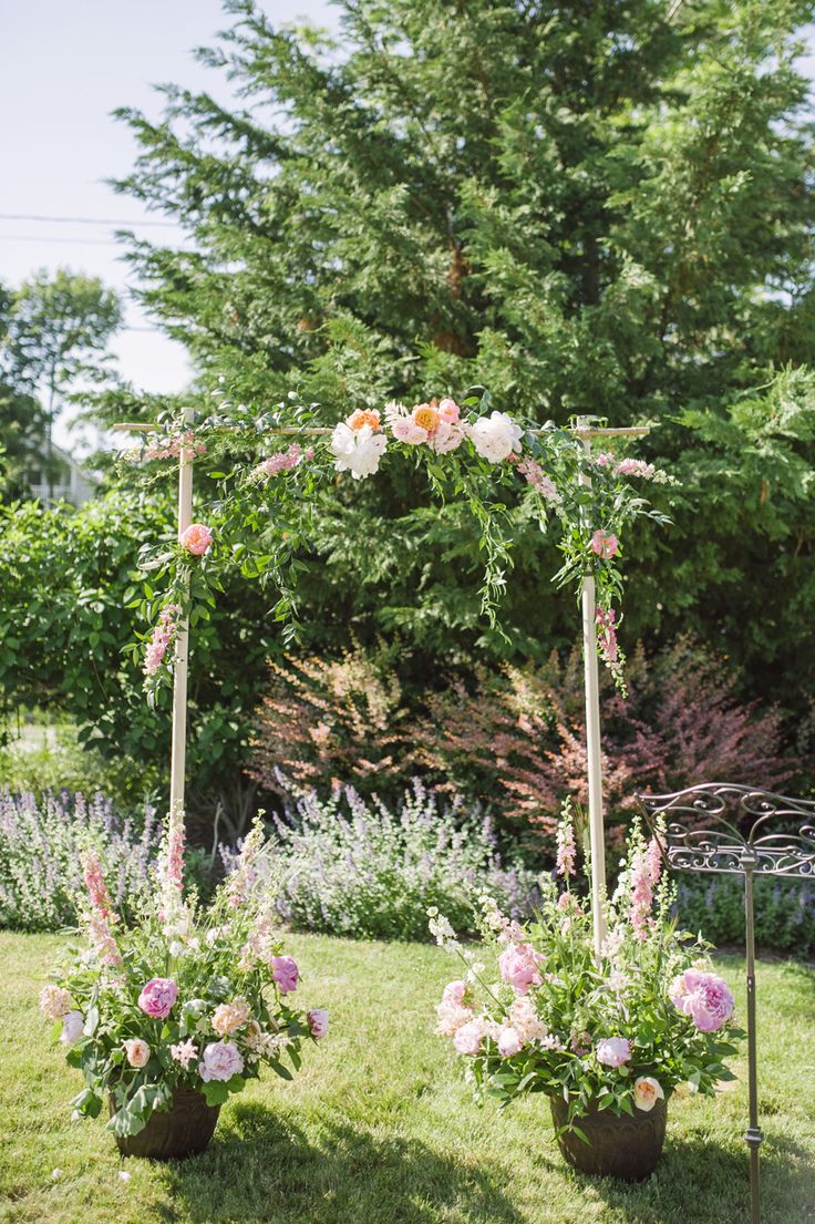 a spring wedding arch of branches decorated with greenery and blooms and put into large pots with flowers