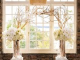 white stands with driftwood branches and lush white florals plus white lanterns create a feeling of a blooming area indoors