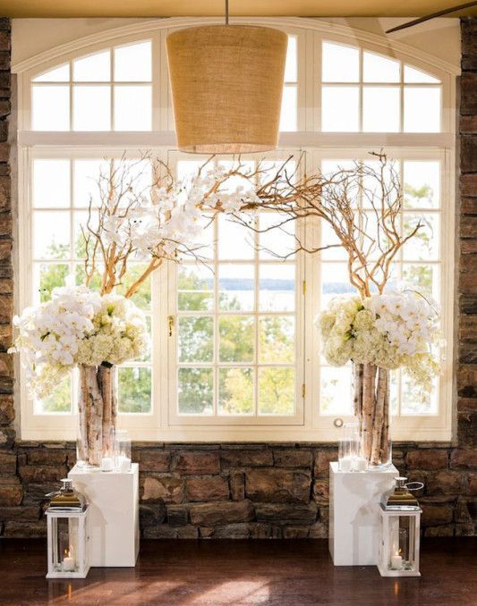 white stands with driftwood branches and lush white florals plus white lanterns create a feeling of a blooming area indoors