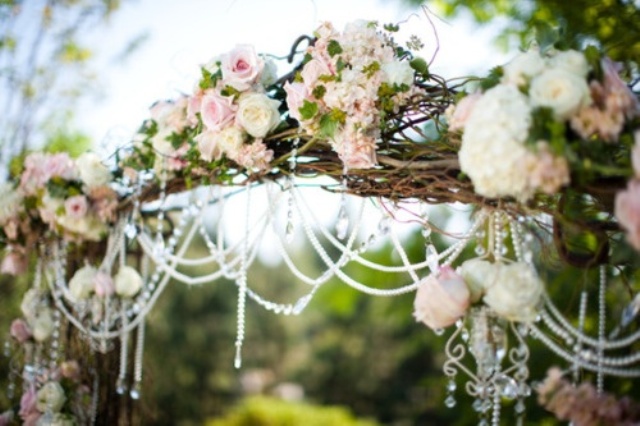 a vine wedding arch decorated with pink and white blooms, with greenery and crystals looks very romantic