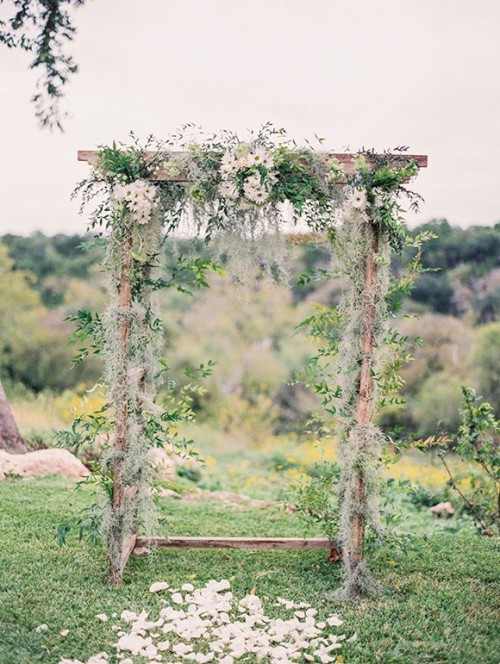 a romantic spring wedding arch with fresh usual and pale greenery, with white blooms on top is a cool idea for a natural touch