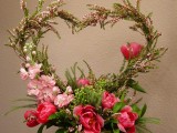 a white centerpiece of greenery, pink blooms and with a large heart in it is a statement and bold decoration to rock