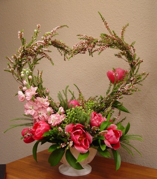 a white centerpiece of greenery, pink blooms and with a large heart in it is a statement and bold decoration to rock
