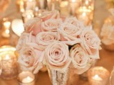 an elegant Valentine’s Day wedding centerpiece of a mercury glass vase and tender blush roses plus candles around is amazing