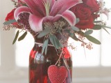 a bold red jar with bold red, pink blooms, eucalyptus and a heart tag is a cool and whimsical idea for a Valentine wedding