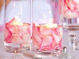 a cluster Valentine centerpiece of tall glasses with pink petals and floating candles is a very fresh and budget-friendly idea