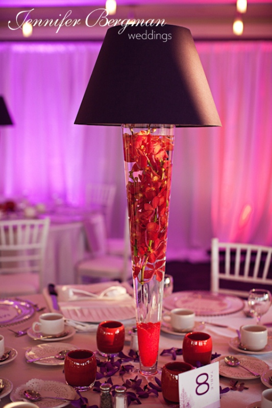 A unique winter wedding centerpiece of a lamp with red blooms floating inside it