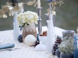 a whimsy and creative winter wedding centerpiece of yarn balls, pinecones, cinnamon bark in a bowl, neutral and gilded blooms