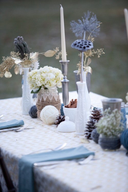 a whimsy and creative winter wedding centerpiece of yarn balls, pinecones, cinnamon bark in a bowl, neutral and gilded blooms