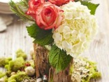a bright rustic winter wedding centerpiece of moss, a tree stump, white hydrangeas and red roses and foliage