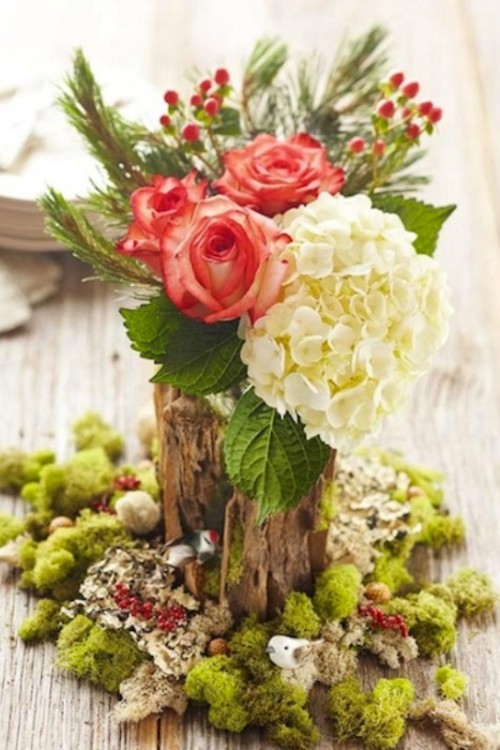 a bright rustic winter wedding centerpiece of moss, a tree stump, white hydrangeas and red roses and foliage