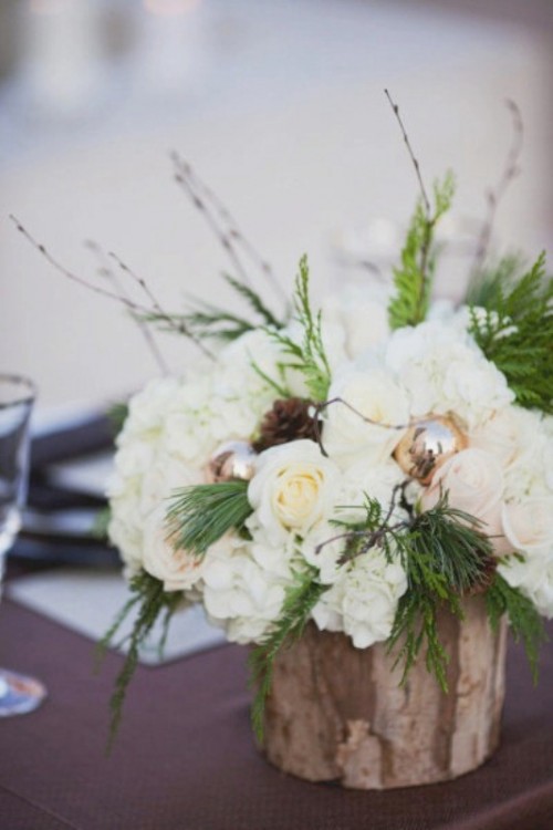 a rustic wedding centerpiece with white blooms, greenery, pinecones and ornaments