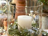 a simple and rustic winter wedding centerpiece in a large candleholder with burlap, evergreens and a pillar candle
