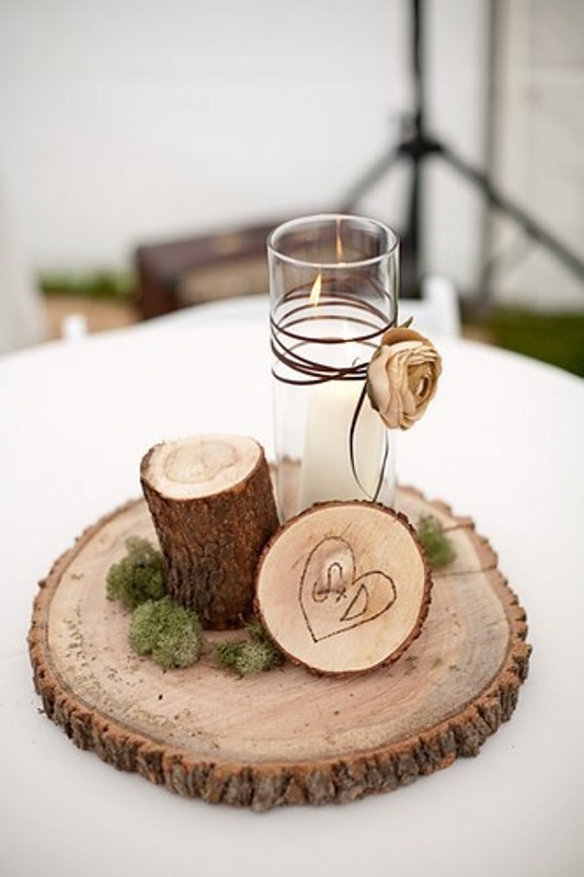 A rustic winter wedding centerpiece of a wood slice, a wood stump, a burnt wood slice and a candle with a fabric bloom