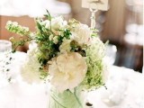 a stylish winter wedding centerpiece of white blooms, greenery and a leaf inside the vase