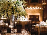 an oversized and lush white floral centerpiece in a tall vase with candles hanging on the branches