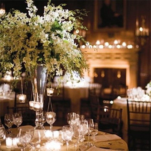 an oversized and lush white floral centerpiece in a tall vase with candles hanging on the branches