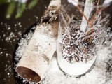 a rustic winter wedding centerpiece of branches and evergreens, snowy pinecones in the vase and bark