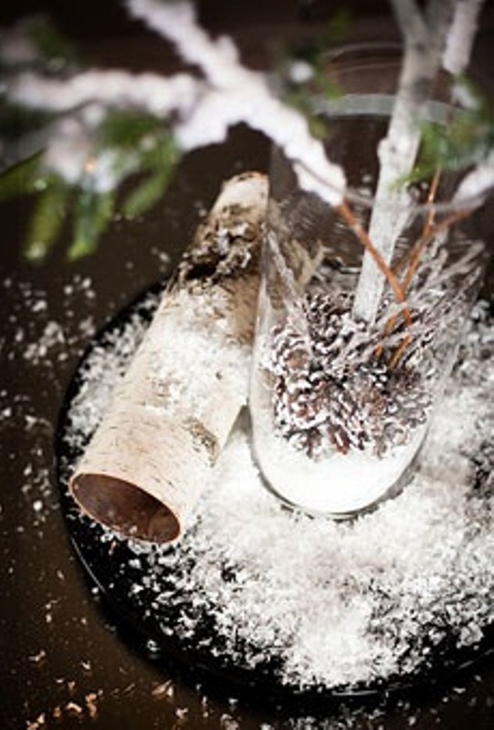 A rustic winter wedding centerpiece of branches and evergreens, snowy pinecones in the vase and bark