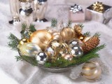 a holiday wedding centerpiece of a bowl with gold and silver ornaments and evergreens