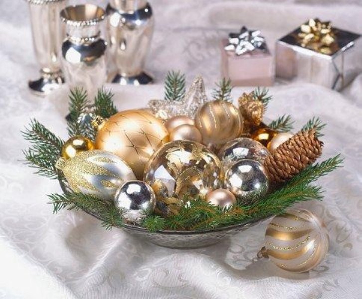 A holiday wedding centerpiece of a bowl with gold and silver ornaments and evergreens