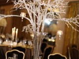 a winter wedding centerpiece of glitter branches in a tall vase and hanging candles on them