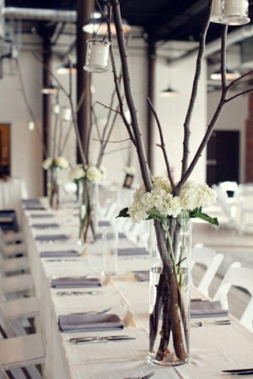 a simple and elegant winter wedding centerpiece of white hydrangeas and tall branches with candles hanging down