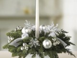 a winter wedding centerpiece of silver ornaments, snowflakes, evergreens and a tall and thin candles