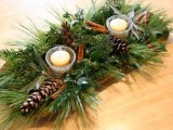 a wooden bowl with evergreens, pinecones, cinnamon sticks, candles and fresh greenery