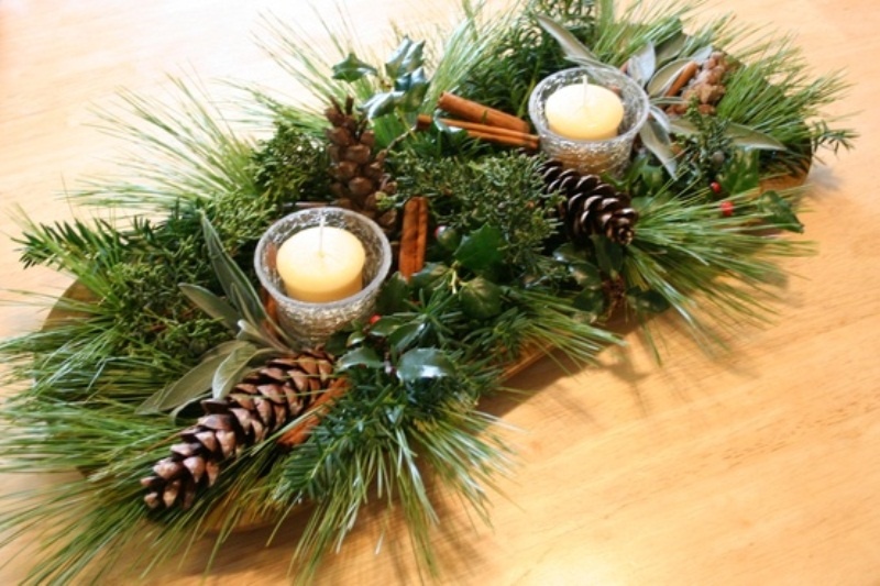 A wooden bowl with evergreens, pinecones, cinnamon sticks, candles and fresh greenery