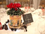 a bold winter wedding centerpiece of red blooms in a large box on a wood slice and pinecones around is a simple and cute idea